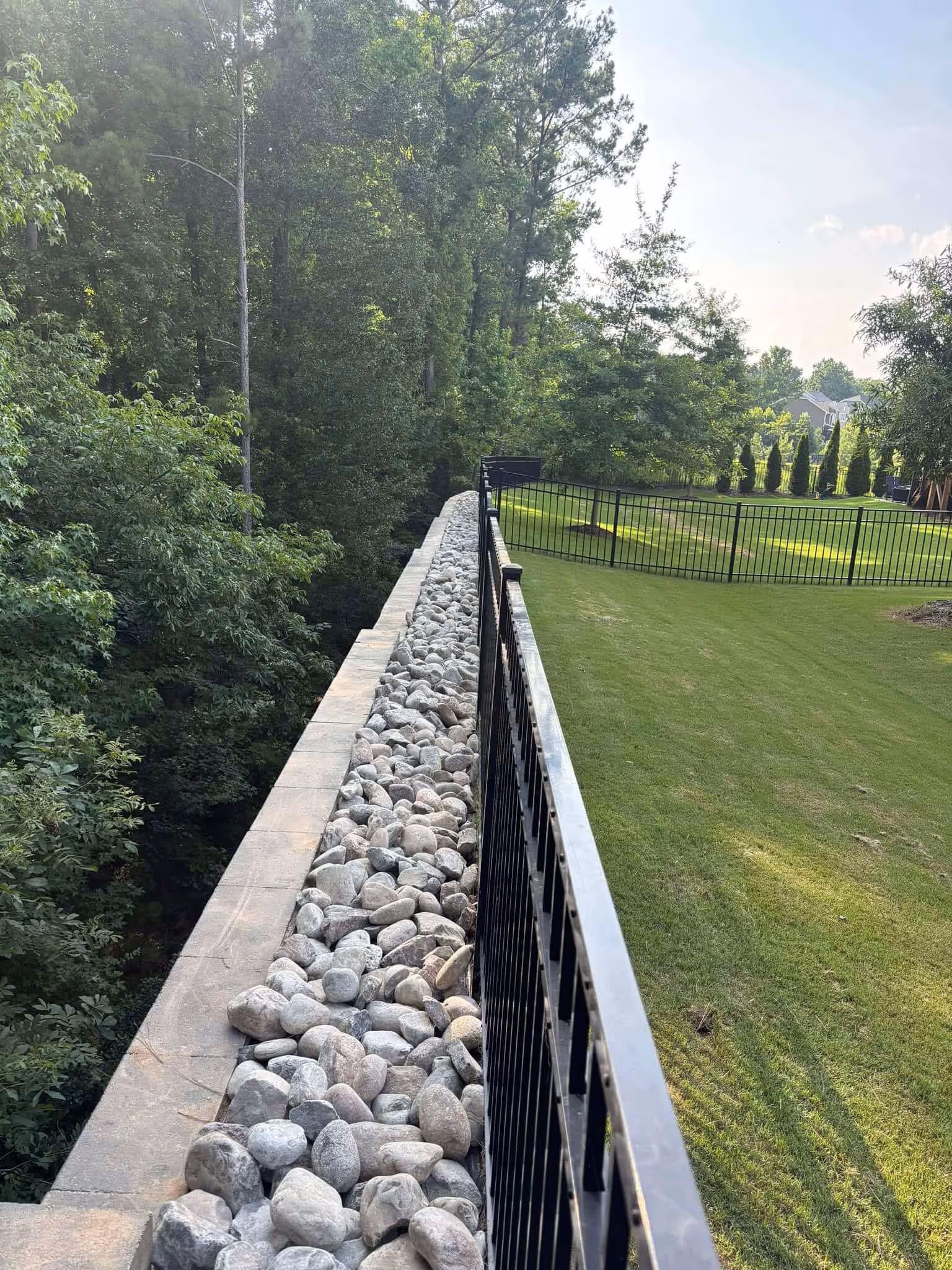 The same retaining wall cleared and capped with a clean row of white river rock along the fence line.