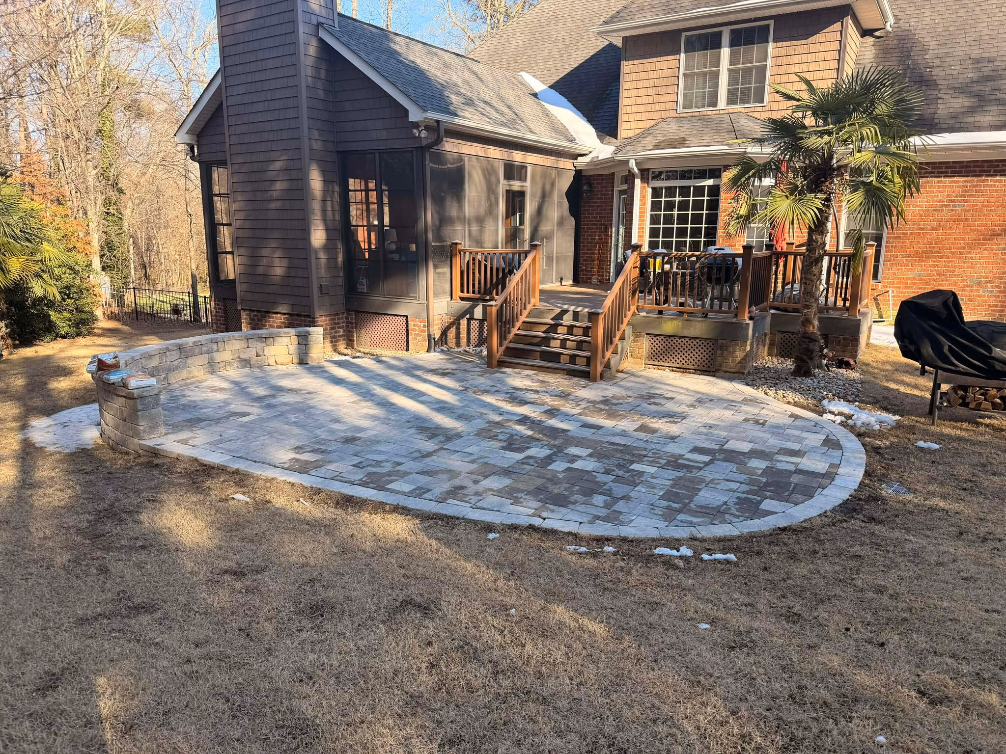 The same backyard finished with a laid paver patio running up to the deck steps.